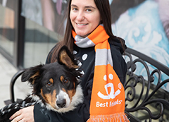 A woman wearing an orange Best Friends scarf with a dog sitting on her lap