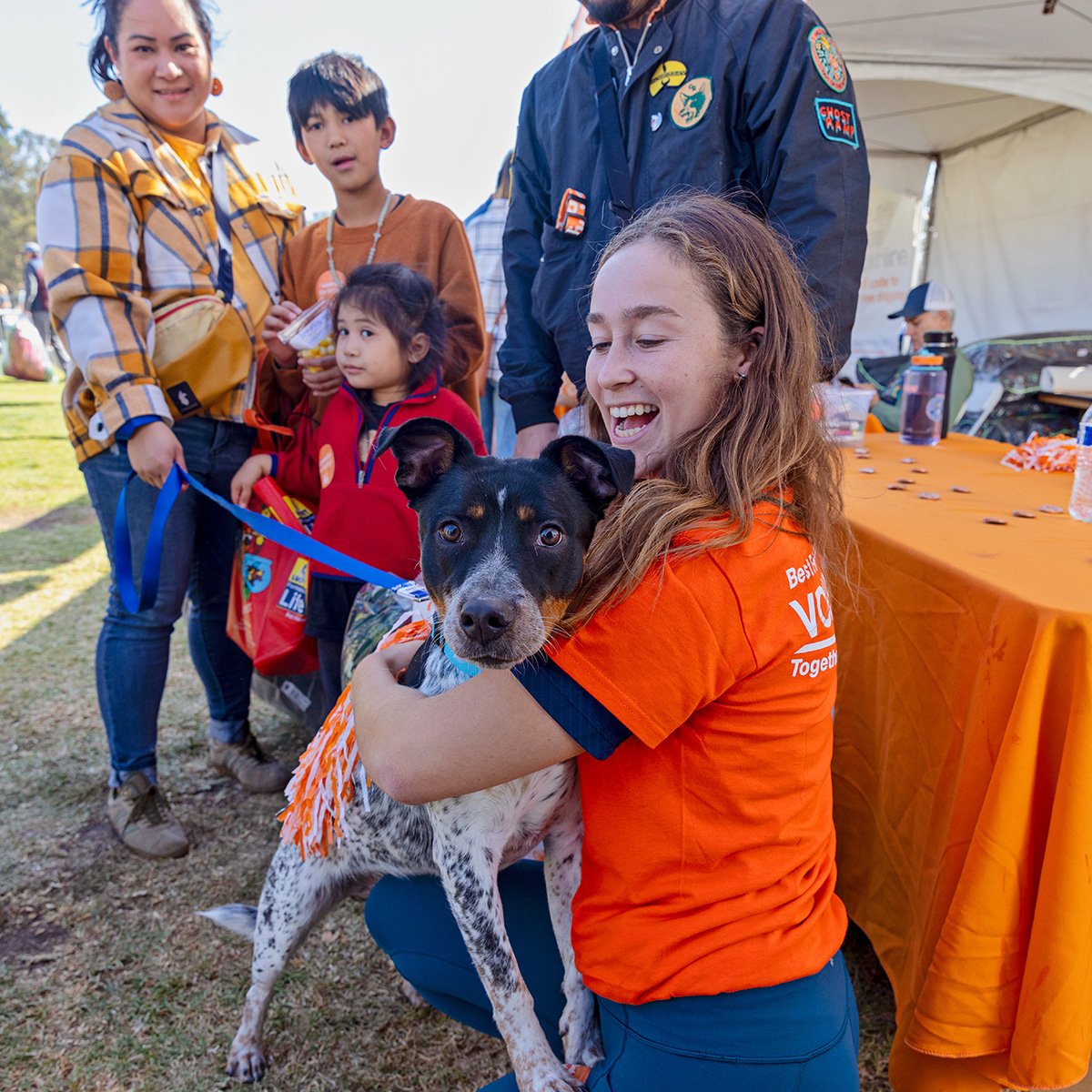 Black and white dog on a leash in a woman's lap with a family behind them